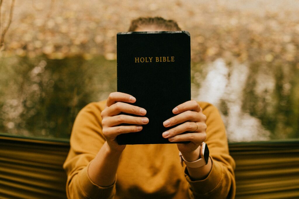 Woman wearing an orange jumper holding and presenting the holy bible